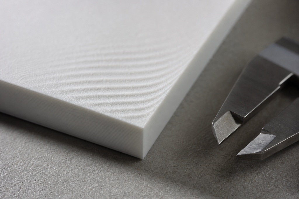 Close-up of a white calibration block and precision caliper on a textured surface for input shaping calibration.