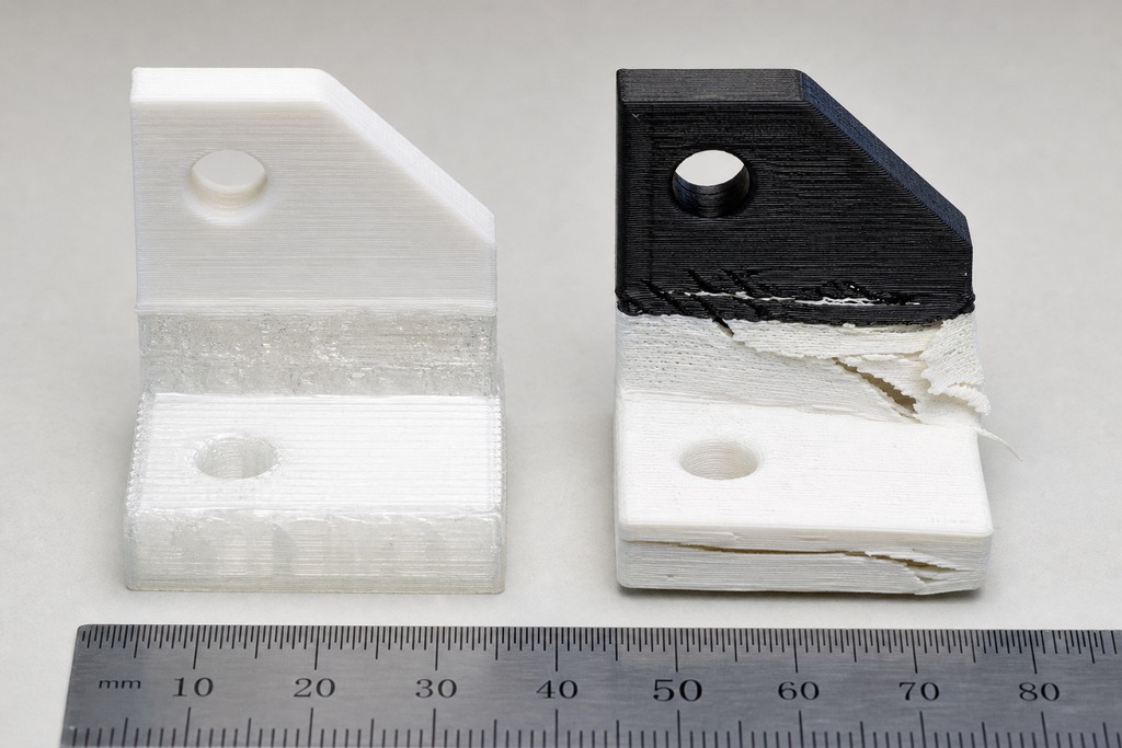 Comparison of two 3D printed multi-material parts, one in white and one in black, showing different textures and finishes.