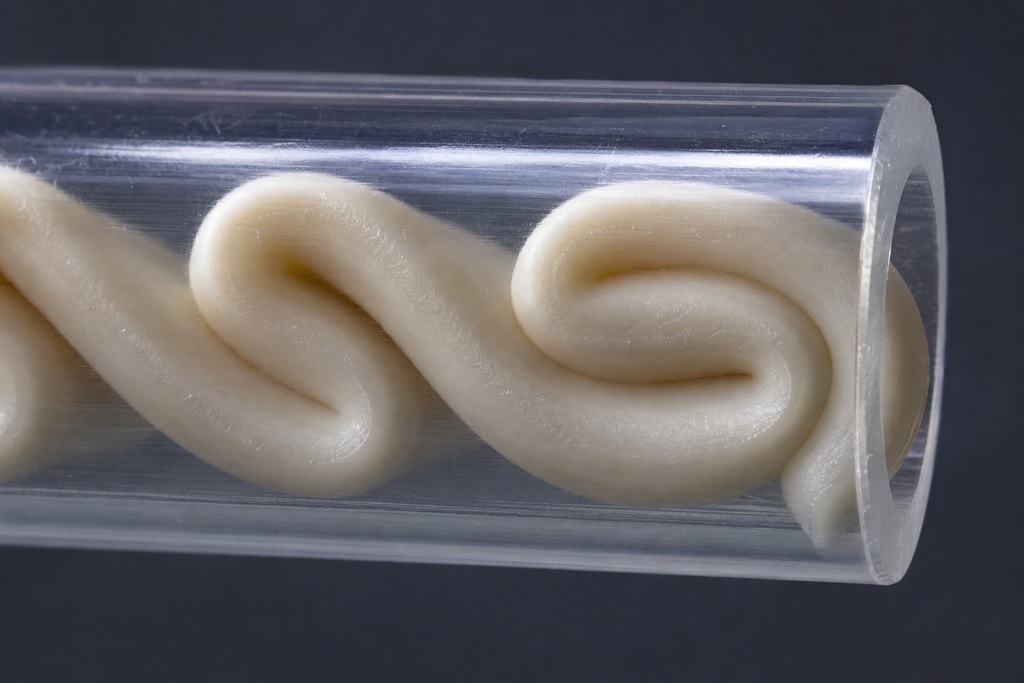 Close-up of smooth, white TPU filament spiraling inside a clear extrusion tube for multi-material printing.