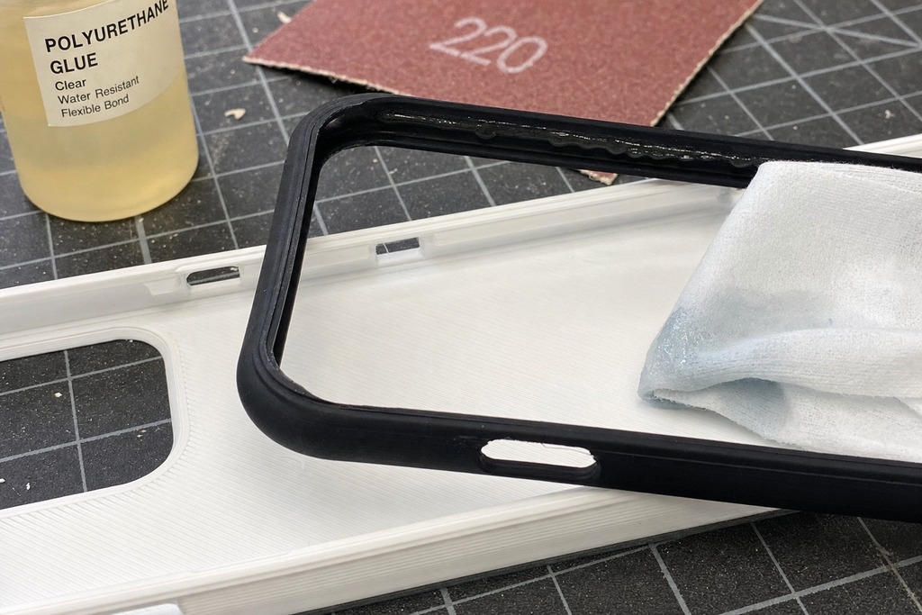 Close-up of TPU and PLA phone case components with polyurethane glue and a cleaning cloth on a work surface.